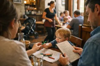 Mother handing a coloring pencil to her young child at a cozy bistro table in Carcassonne, with a relaxed, authentic family atmosphere and gentle afternoon light.